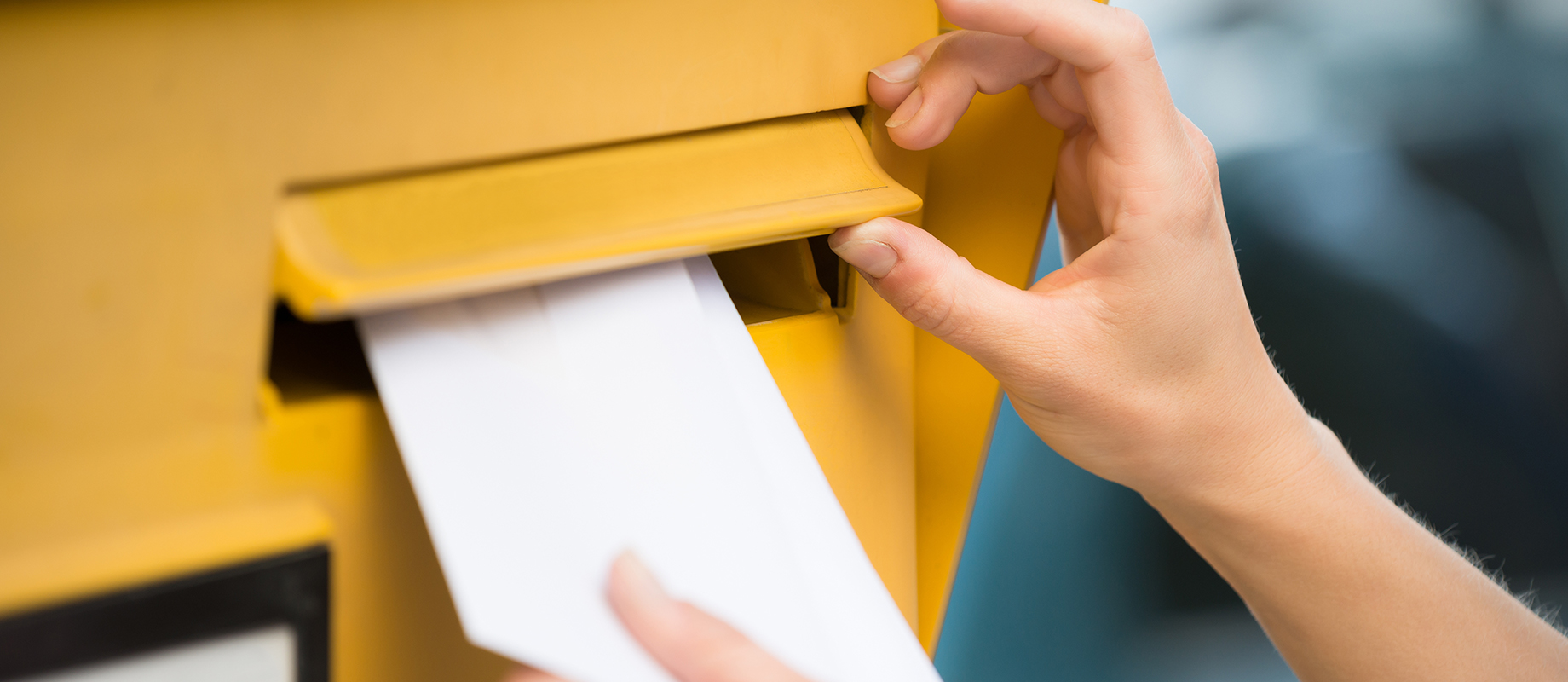 Une lettre est déposée dans une boîte aux lettres jaune