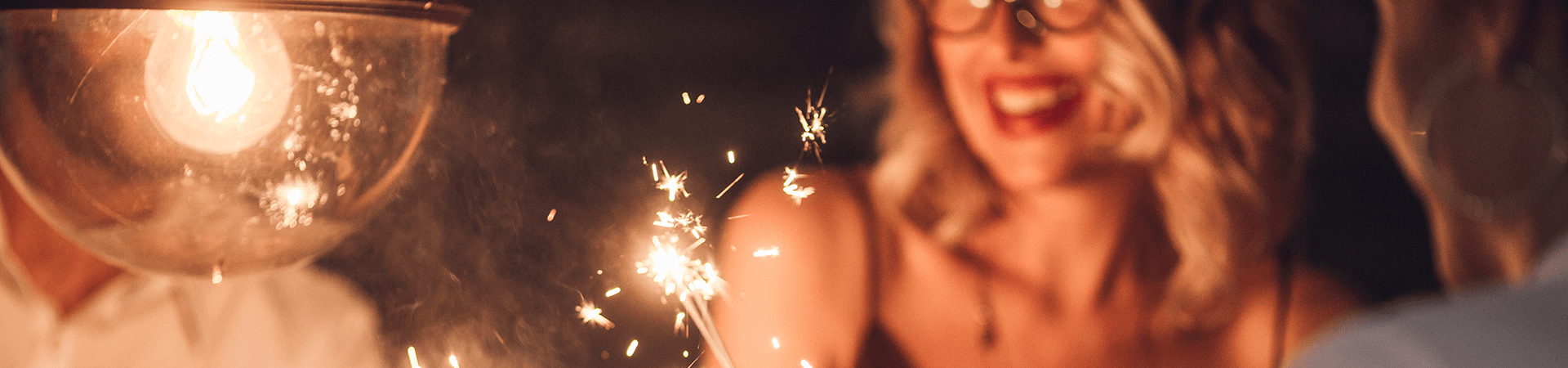 Une femme sourit en regardant les éteincelles de bougies d'anniversaire