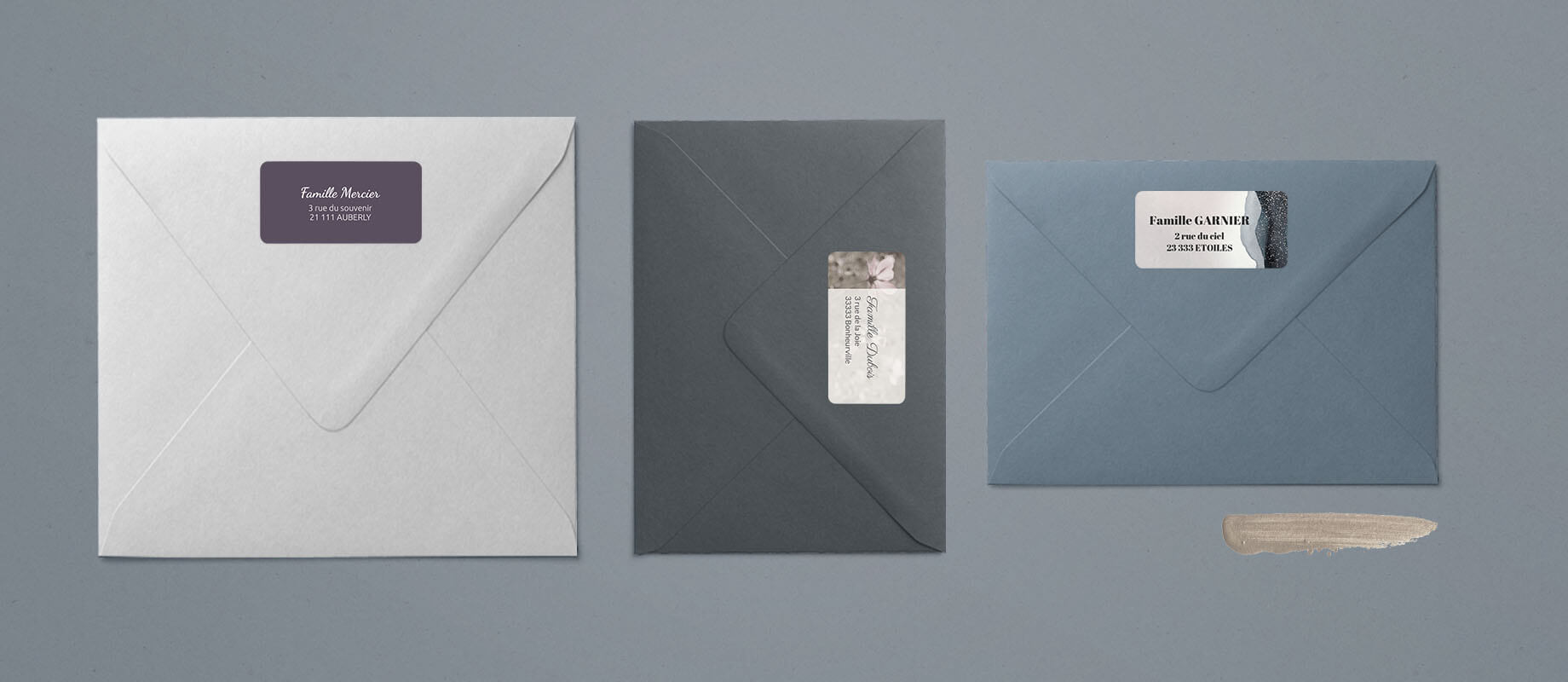 Une enveloppe grise, une enveloppe bleue, une enveloppe blanche accompagnées de leur étiquette d'adresse collée à l'arrière des enveloppe.