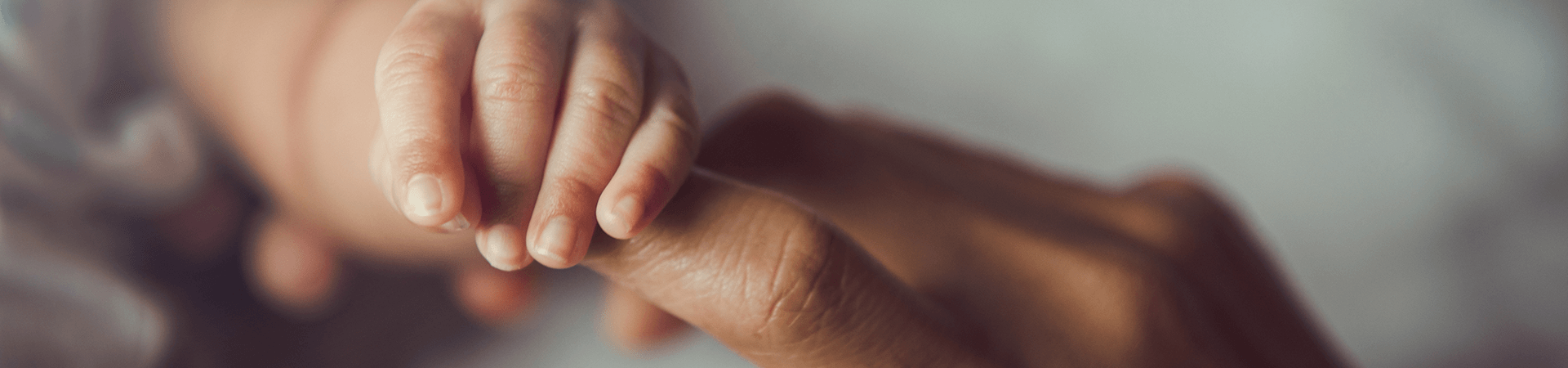Une main de bébé attrape le doigt d'une main d'adulte