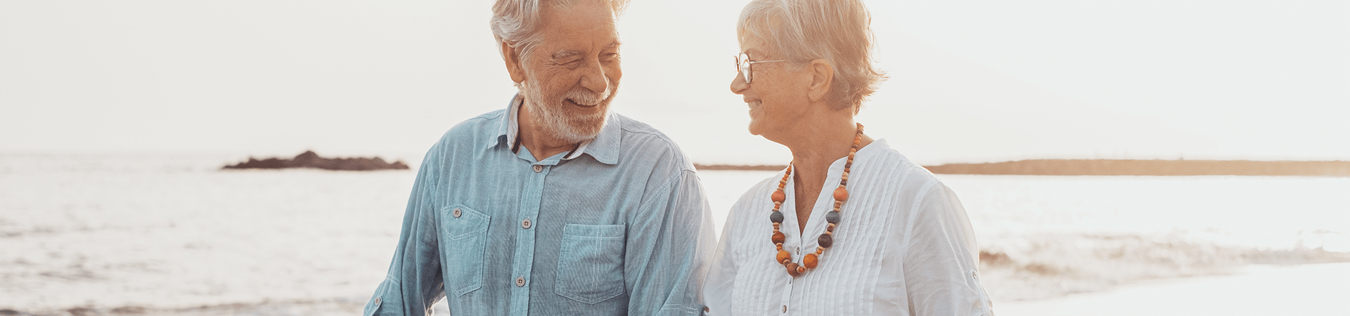 Un couple retraités souriants marche sur la plage